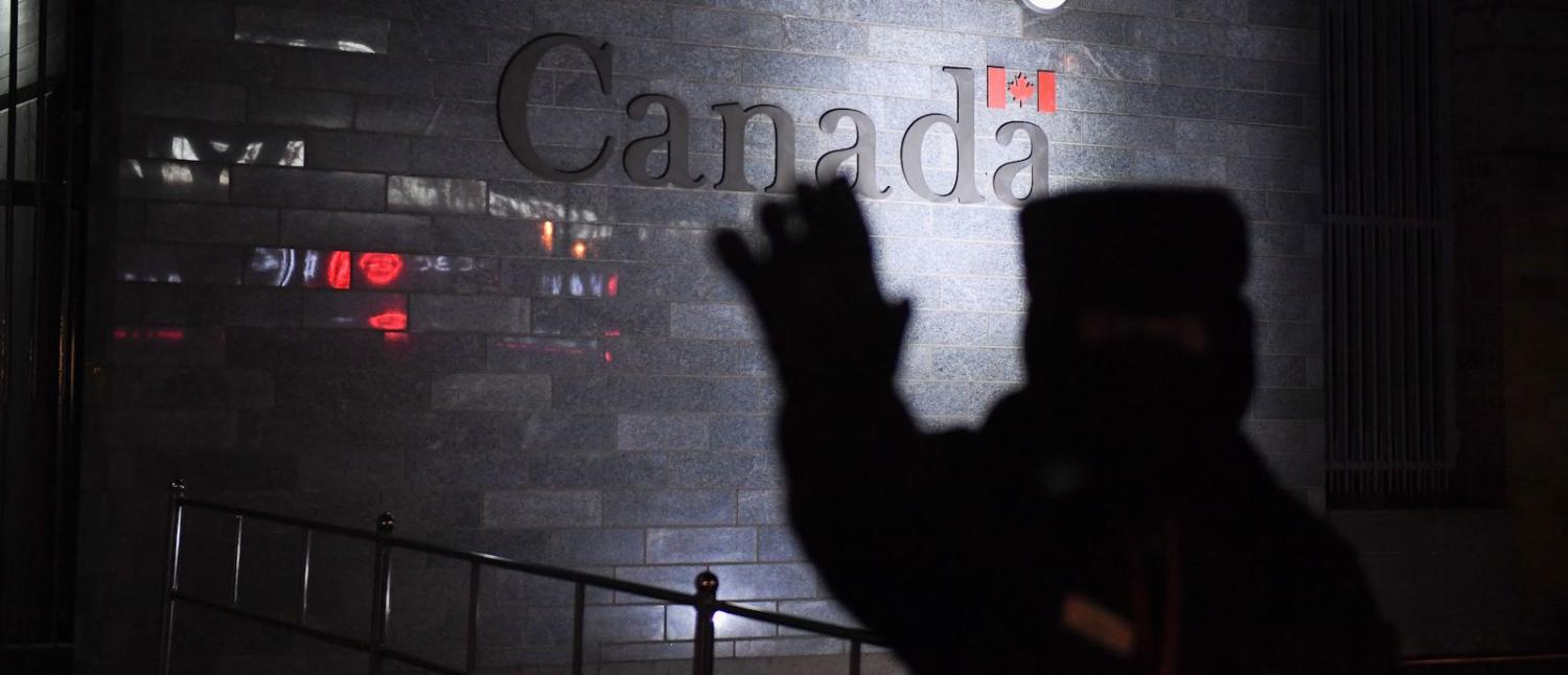 A guard tries to block photos being taken as he patrols outside the Canadian embassy in Beijing on 14 January (Photo: Greg Baker via Getty)